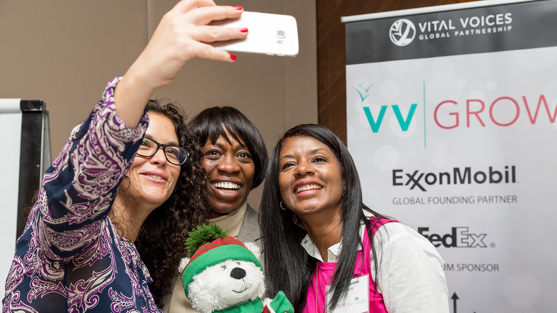 three women are taking a picture with a teddy bear at an event.