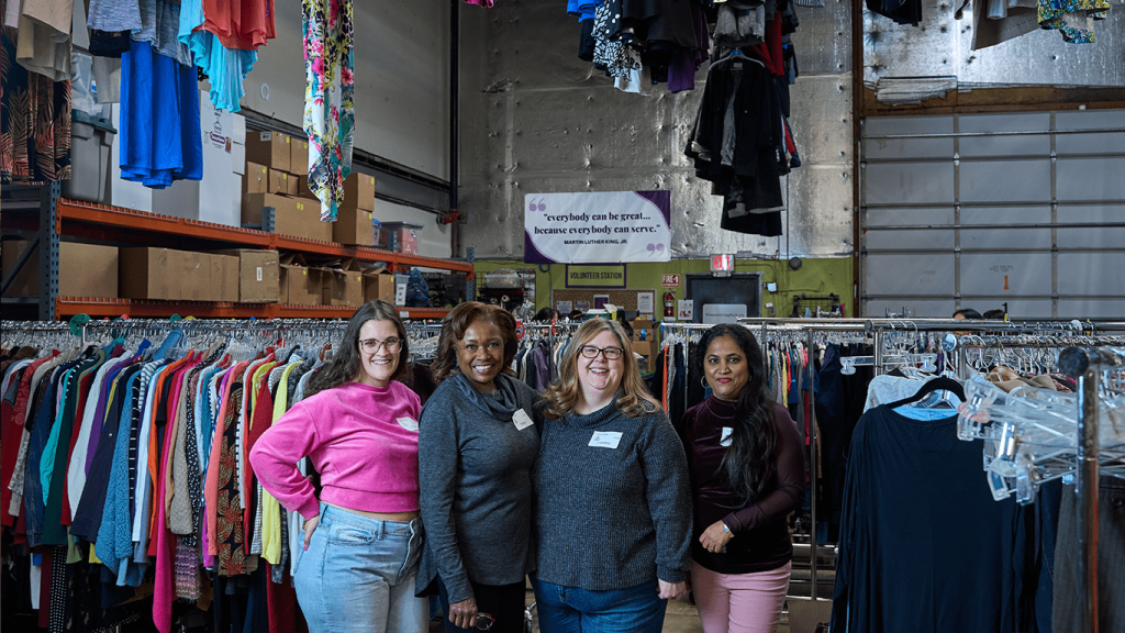 four women standing in front of racks of clothes.