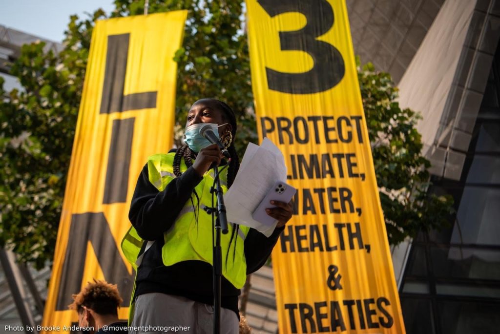 a man in a yellow vest is speaking at a protest.