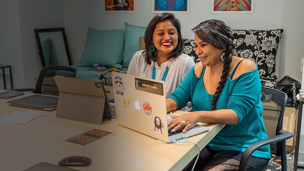 two women sitting at a table with laptops in front of them.