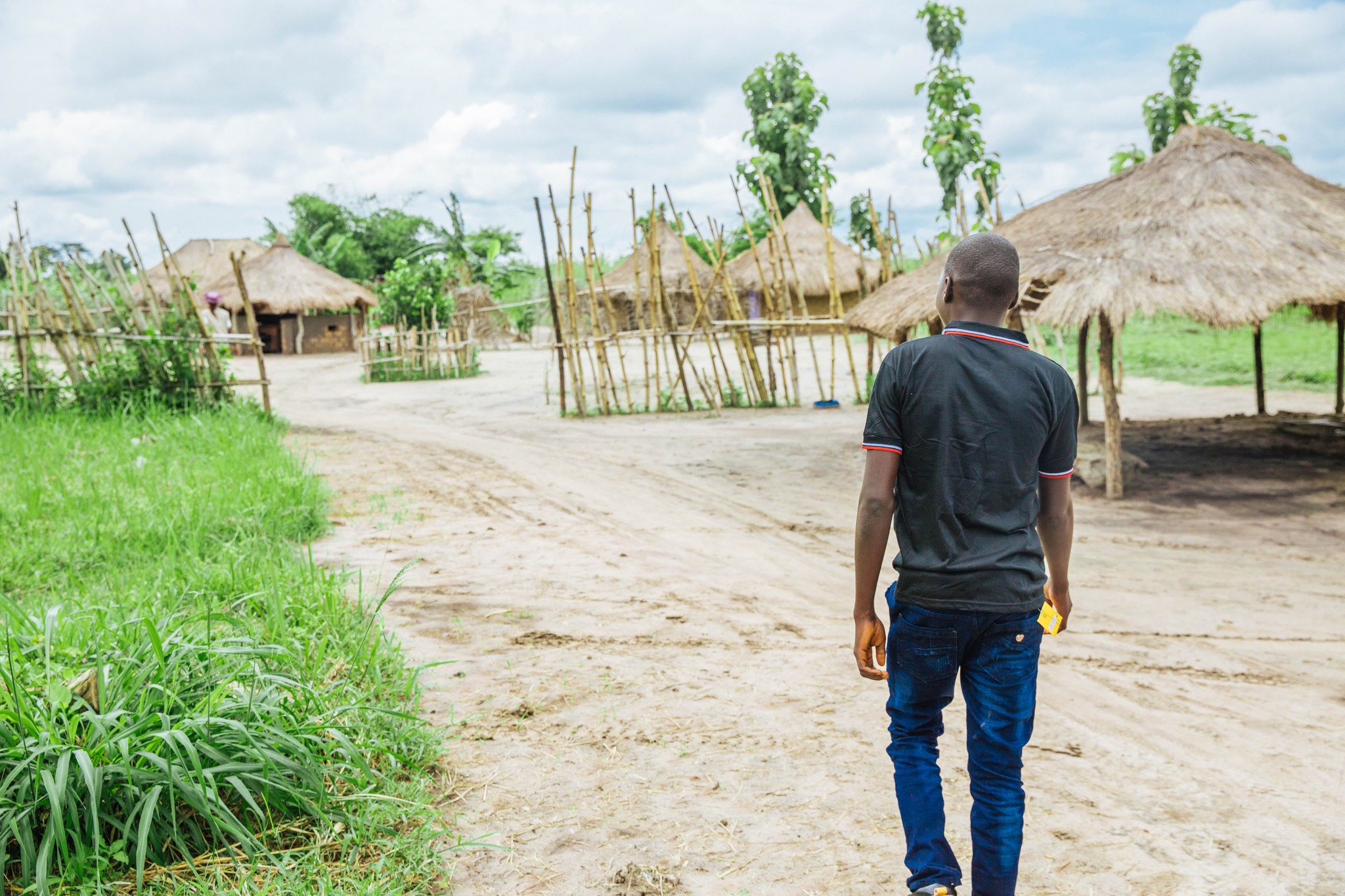 a man walking down a dirt road with thatched huts.