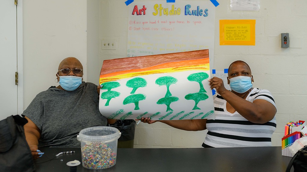 two women wearing face masks holding up a drawing.