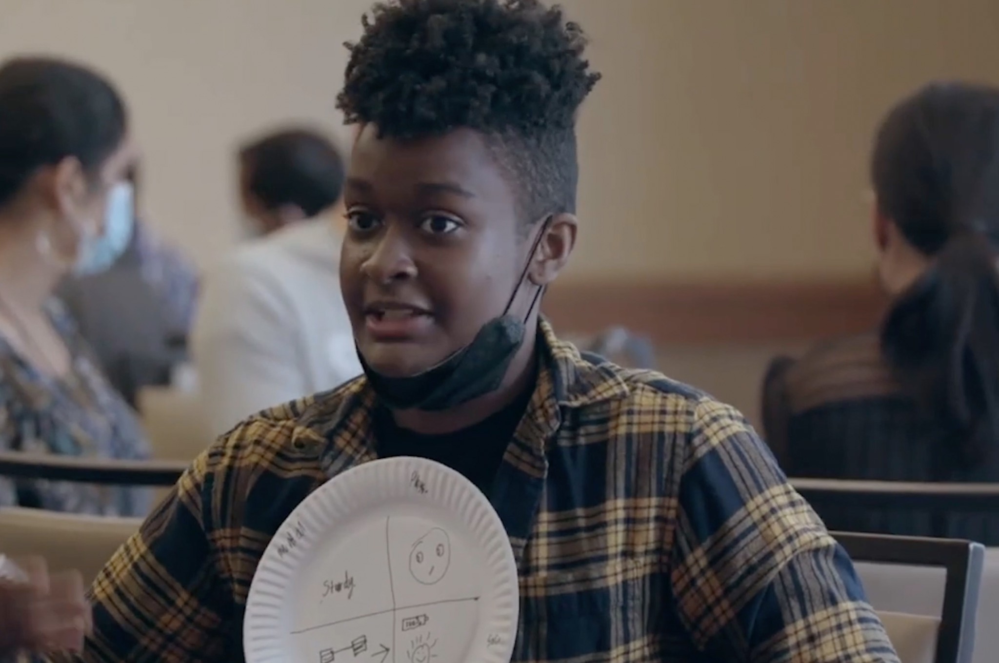 a young girl holding a paper plate in front of a group of people.