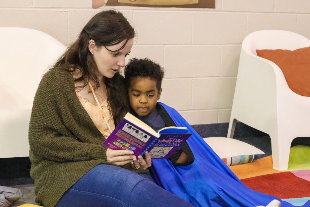 a woman reading a book to a child in a classroom.