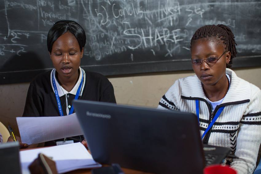 three women sitting at a desk with laptops in front of them.