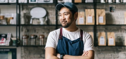 a man in a hat and apron standing in front of a coffee shop.