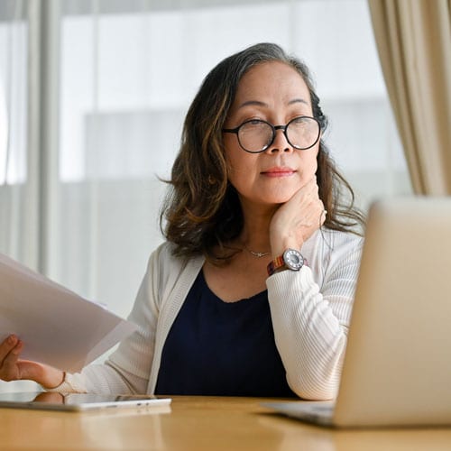 Professional woman reviewing documents at a computer desk.