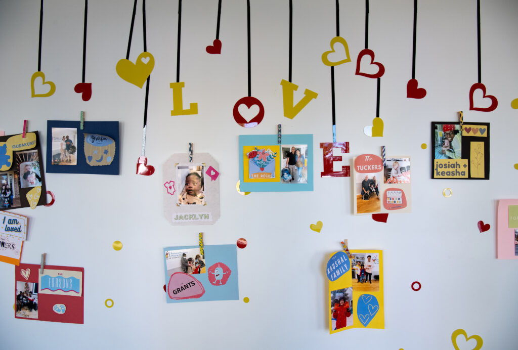 A wall adorned with colorful cards and photos clipped on black ribbons. The decorations include hearts and the word "LOVE". Names like "JACOLYN" and "KEESHA" are visible on the cards.